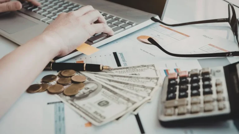 Como organizar seu dinheiro do zero - Uma pessoa no computador com uma calculadora do lado.